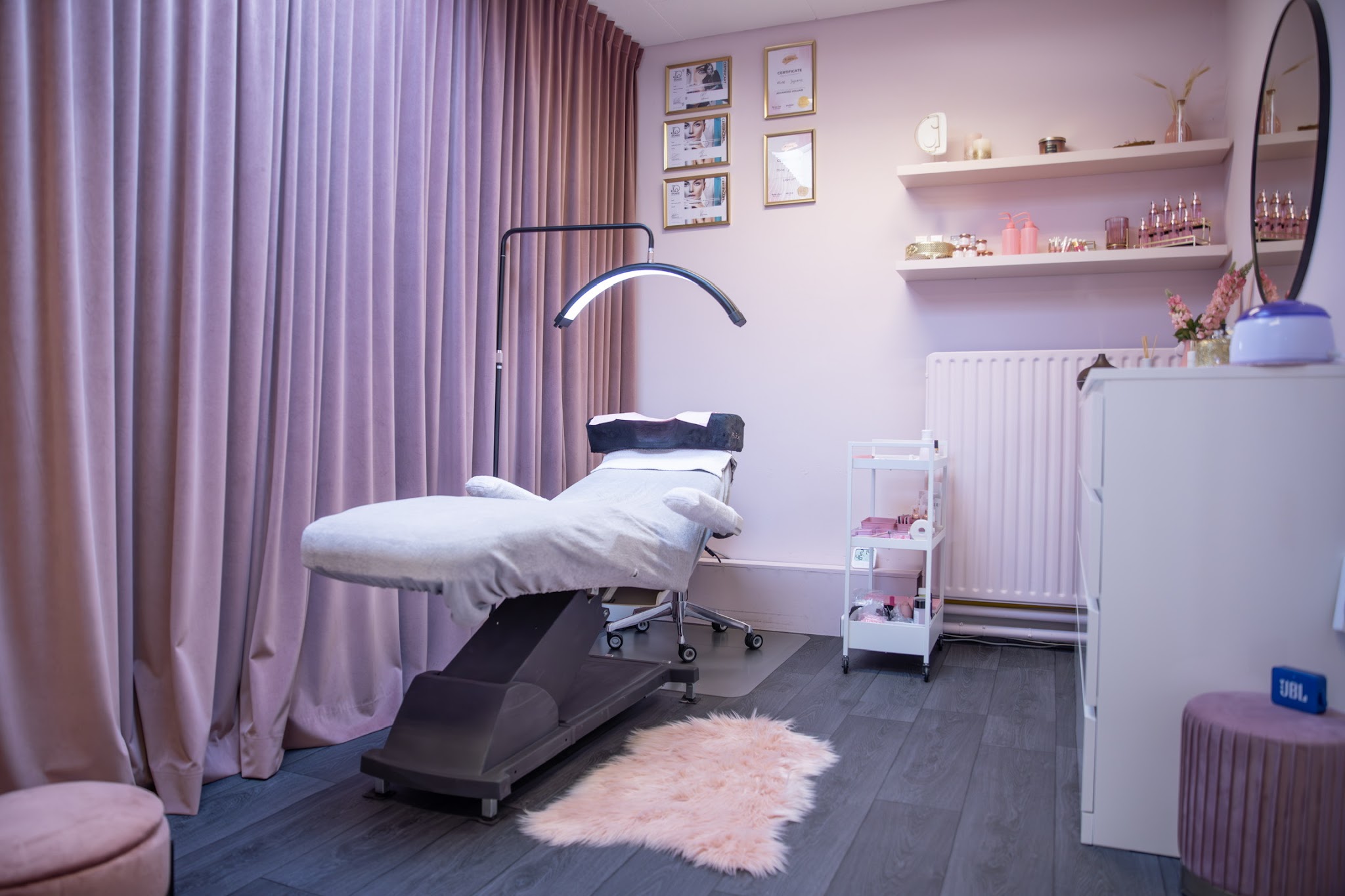 De behandelruimte: verstelbaar bed, LED-lamp, mauve fluwelen gordijnen en een kast met producten
