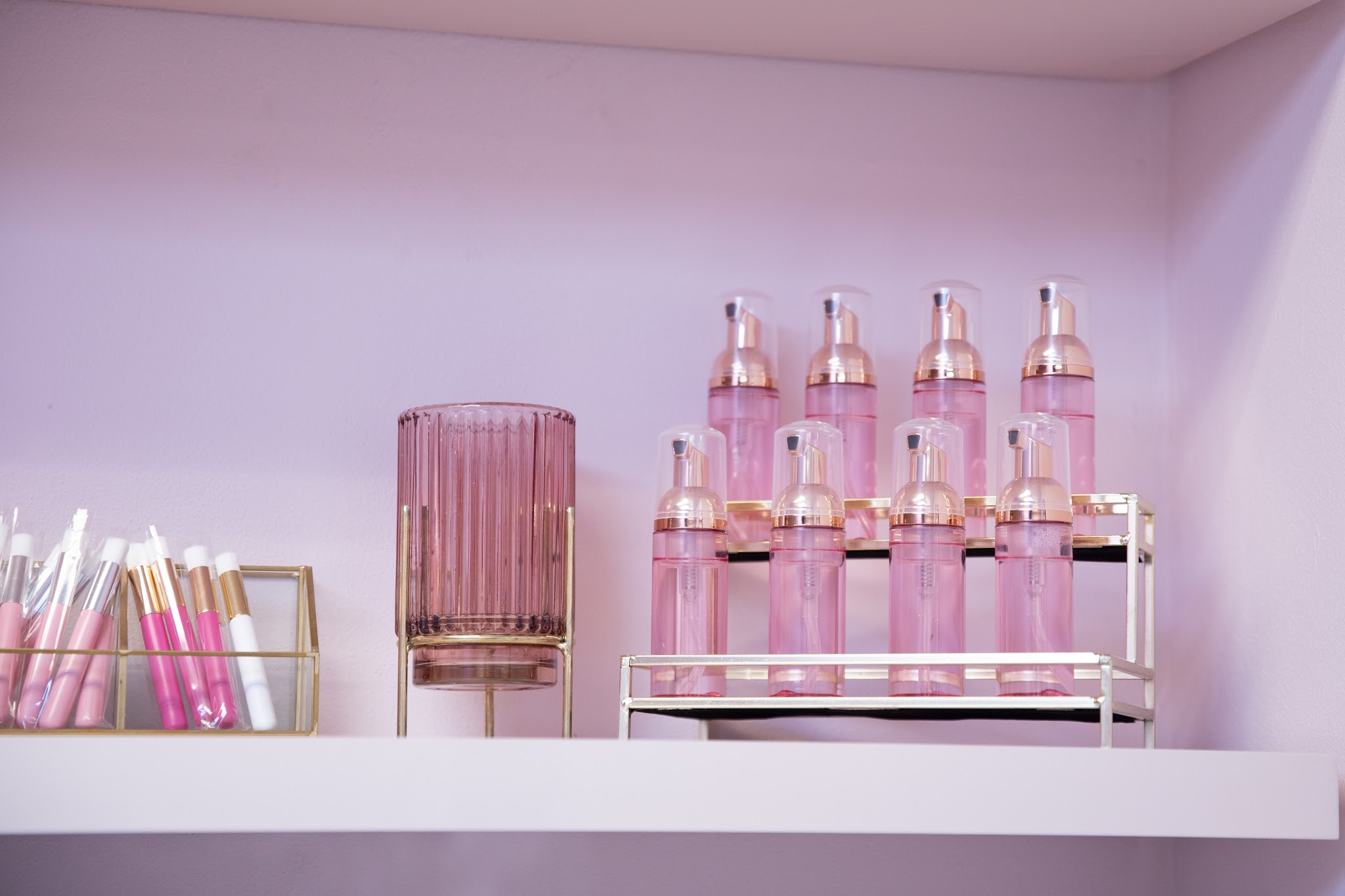 Roze flesjes foamreiniger en wimperborsteltjes op een plank