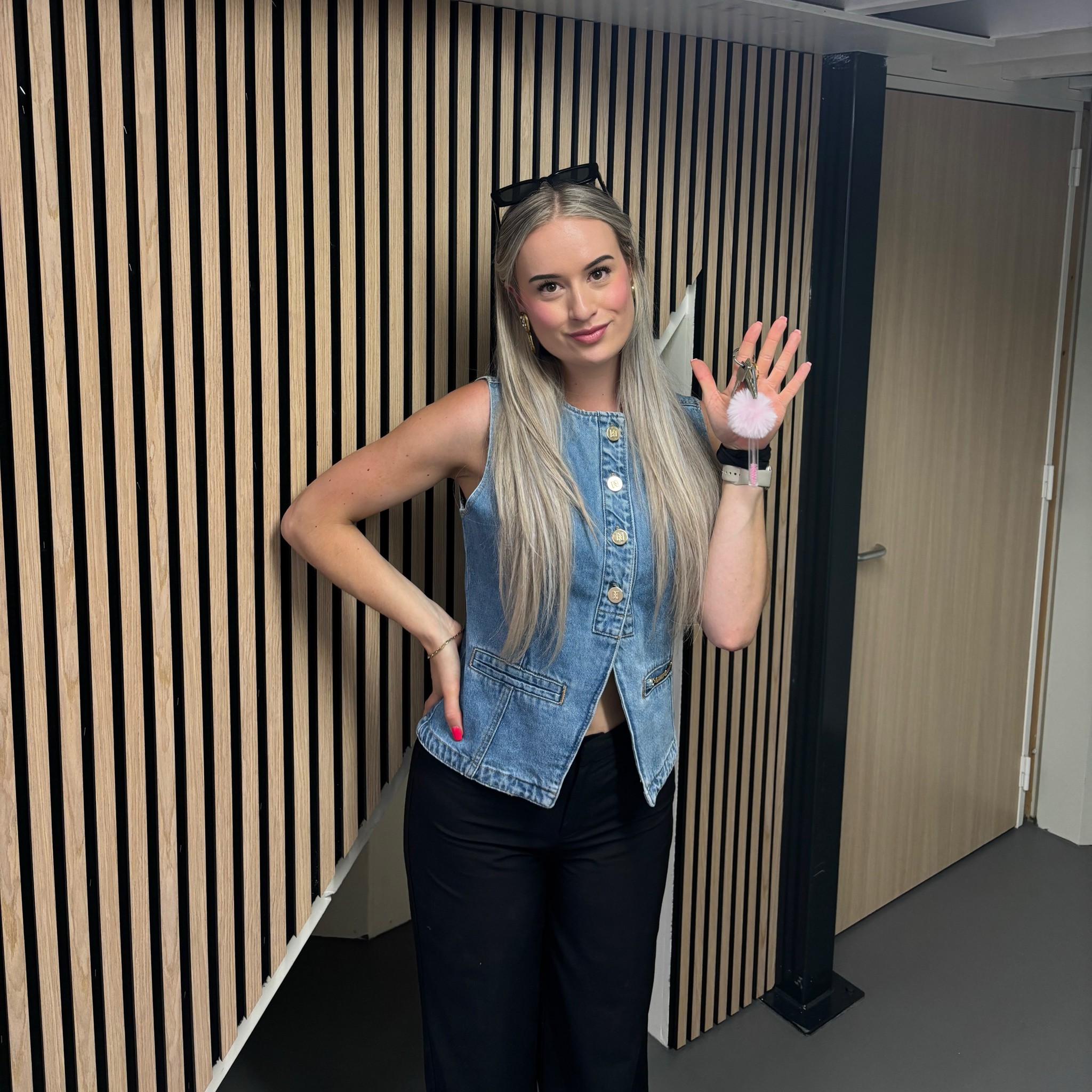 Mirte zwaait in de gang van het nieuwe pand, met een wand van houten latten